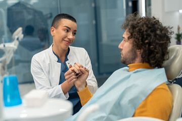 Supportive female dentist professional holding patient's hand on dentist's chair who's feeling...