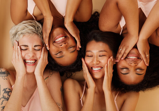 Happy girls touching their faces while lying together on a beige background. Smiling women with closed eyes massaging their cheeks with palms.