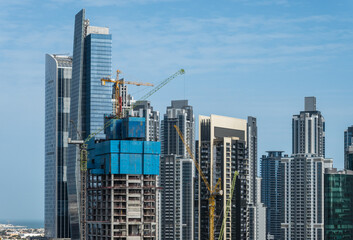 Fototapeta na wymiar Cranes surround the construction of new tower for apartments along canal in Business Bay Dubai UAE