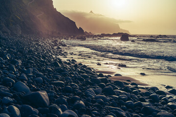 une plage de galets au pieds de falaise sous un coucher de soleil en contre jour jaune