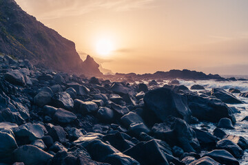 Des falaises en bord d'océan sous un coucher de soleil orange et une plage de rochers