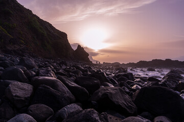 une plage de rochers au pieds de falaises sous un coucher de soleil pourpre