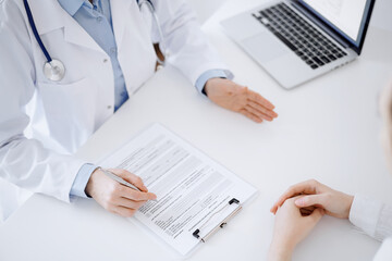 Doctor and patient discussing current health questions while sitting opposite of each other and using clipboard at the table in clinic, just hands closeup. Medicine concept