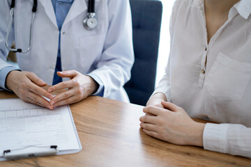Doctor and patient discussing something while sitting near each other at the wooden desk in clinic, view from above. Medicine concept