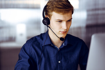 Young blond businessman using headset and computer at work. Startup business means working hard and out of time for success achievement