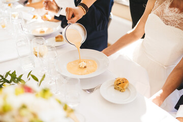A close up of a person pouring soup into a plate at a wedding.