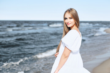Fototapeta na wymiar Happy, beautiful woman on the ocean beach standing in a white summer dress