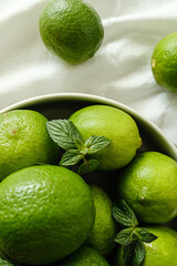 vários limões verdes dentro de prato cinza sobre mesa com tecido branco com folha de hortelã