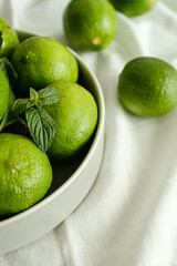 limão verde dentro de prato cinza sobre mesa com tecido branco com folha de hortelã