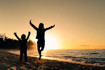 Fototapeta premium Happy little boy and girl kids playing jumping for joy on the beach having summertime fun 