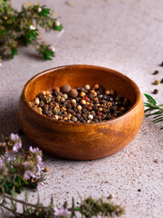 cuenco de madera con tres pimientas decorado con flores en fondo gris de piedra