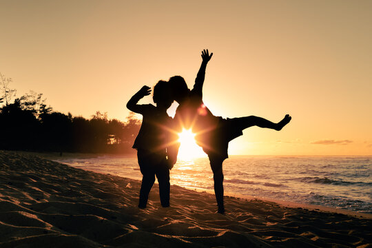 Happy little boy and girl kids playing jumping for joy on the beach having summertime fun	