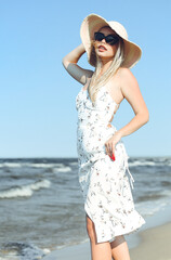 Happy blonde woman in free happiness bliss on ocean beach standing with sun glasses and hat