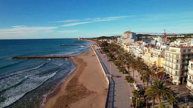 Drone flight back over in along coast beautiful beaches surrounded by Palm trees in Sitges. Mediterranean landscape of beach and hotels. Gentle sea waves quietly roll onto shore. Film intro. 4K video