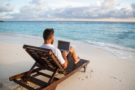 man working on laptop on tropical beach