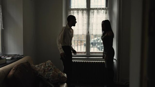 Silhouettes of a couple fighting by window at home. Young man throwing jacket into couch feeling nervous and anger at female partner. People shouting at each other