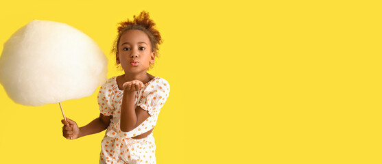 Little African-American girl with cotton candy sending air kiss on yellow background with space for space