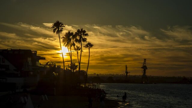 4K Timelapse of the sunset over Coronado Island in San Diego, California behind the silhouettes of palm trees and Navy vessels from the military naval bases nearby. 