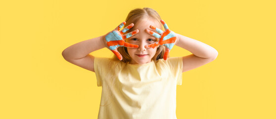 Funny little girl with palms in paints on yellow background