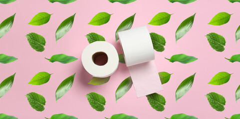 Rolls of toilet paper and many green leaves on pink background