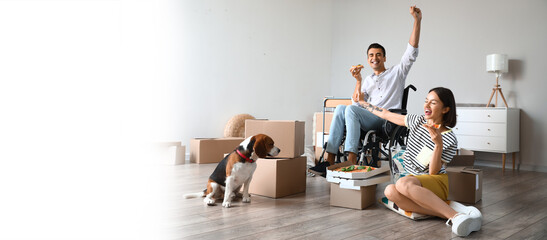 Young woman with her husband in wheelchair and with dog eating pizza in their new home on moving...