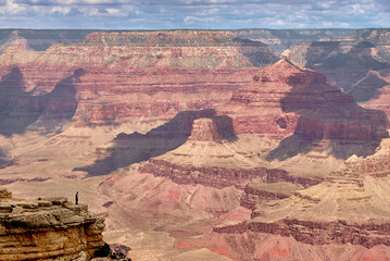 A solitary man standing on a rocky outcropping looking out over the Grand Cayon at Mather Point on the south rim of the canyon in Arizona, USA.