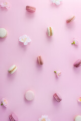 Fototapeta na wymiar Macaroons of different flavors and flowers on a pink background. Vertical pastel pattern, selective focus