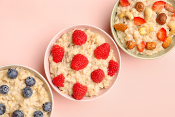 Bowls with tasty oatmeal, blueberries, raspberries and nuts on pink background