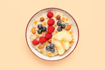 Bowl with tasty oatmeal, ripe berries, nuts, raisins and apple on beige background