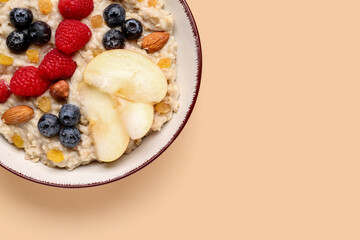 Bowl with tasty oatmeal, ripe berries, nuts, raisins and apple on beige background