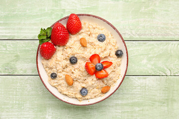 Bowl with tasty oatmeal, almonds, blueberries and strawberries on green wooden background