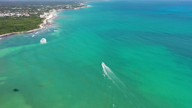 Aerial landscape view of an parasailing parachute inflight - pulled by a speedboat sailing in turquoise water near a tropical coastline - aerial video footage