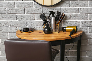 Different hair sprays and accessories on table near grey brick wall