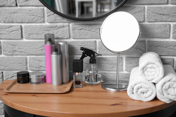 Different hair sprays and accessories on table near grey brick wall