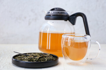 Cup of hot green tea and dry leaves on light background