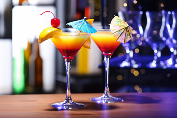 Glasses of tasty Tequila Sunrise with umbrellas on table in bar