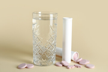 Glass of water and tubes with soluble tablets on color background