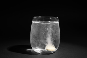 Glass of water with soluble tablet on dark background