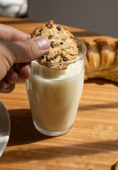 holding a homemade chocolate chip cookie to dip into a glass of fresh milk, food and drink, close up of glass, textures
