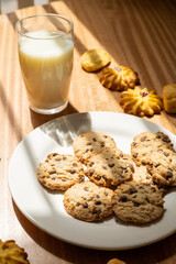 details of a restaurant table with a glass of milk next to chocolate chip cookies, delicious drinks and home baked food, appetizing snack
