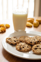 glass of milk next to a plate with chocolate chip cookies, delicious drinks and home baked food, appetizing snack