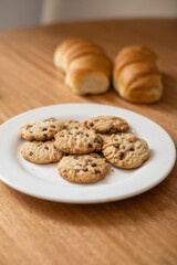 plate with cookies decorated with chocolate chips, sweet and healthy food, texture in studio, homemade snack with breads in the background, pastry shop