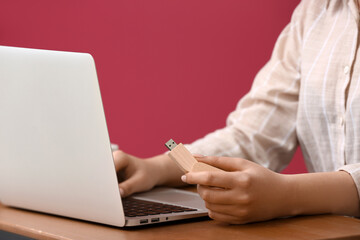 Naklejka premium Woman using USB flash drive with modern laptop at wooden table near color wall, closeup