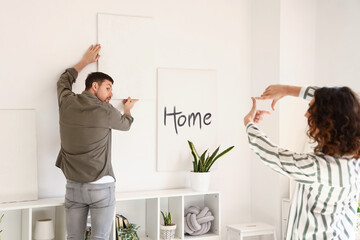 Young couple hanging painting on light wall at home