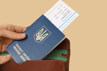 Woman putting Ukrainian passport with ticket in wallet on beige background, closeup