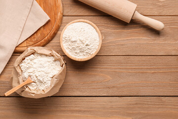 Composition with bowl of wheat flour, bag and rolling pin on wooden table