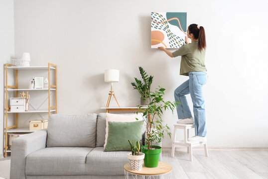 Young woman hanging picture on wall in living room
