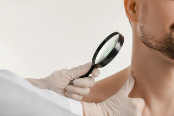 Dermatologist examining mole of young man with magnifier on white background, closeup