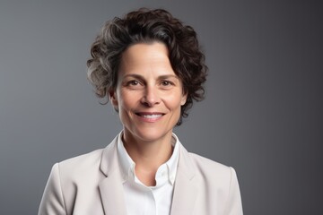 Medium shot portrait photography of a grinning woman in her 40s wearing a classic blazer against a gray background. Generative AI