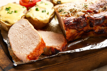 Wooden board with tasty baked meat and potatoes, closeup